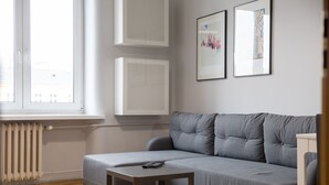 Ein modernes Wohnzimmer mit einer grauen Couch, einem kleinen Tisch und einer Heizung. An der Wand hängen zwei gerahmte Bilder.