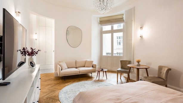 Une chambre moderne avec un grand lit, une télévision, un canapé, un fauteuil, une petite table et une grande fenêtre.