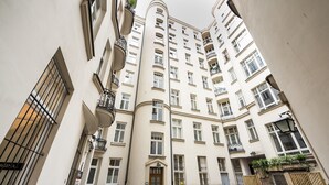 Une rue étroite en milieu urbain, bordée d’un immeuble résidentiel imposant, doté de nombreux balcons et d’une entrée centrale.