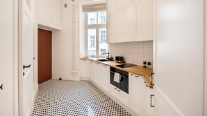 Une cuisine étroite avec des meubles blancs, un carrelage noir et blanc et une fenêtre qui laisse entrer la lumière naturelle.