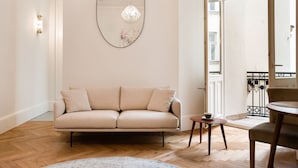 Un salon moderne avec un canapé beige, un miroir rond, un lustre et un plancher en bois.