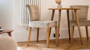 Une pièce comprenant deux fauteuils rembourrés, une petite table en bois, un luminaire fixé au mur et un radiateur.