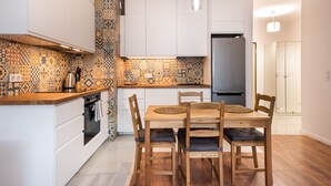 A modern kitchen with patterned backsplash, white cabinets, and a wooden dining table with chairs.
