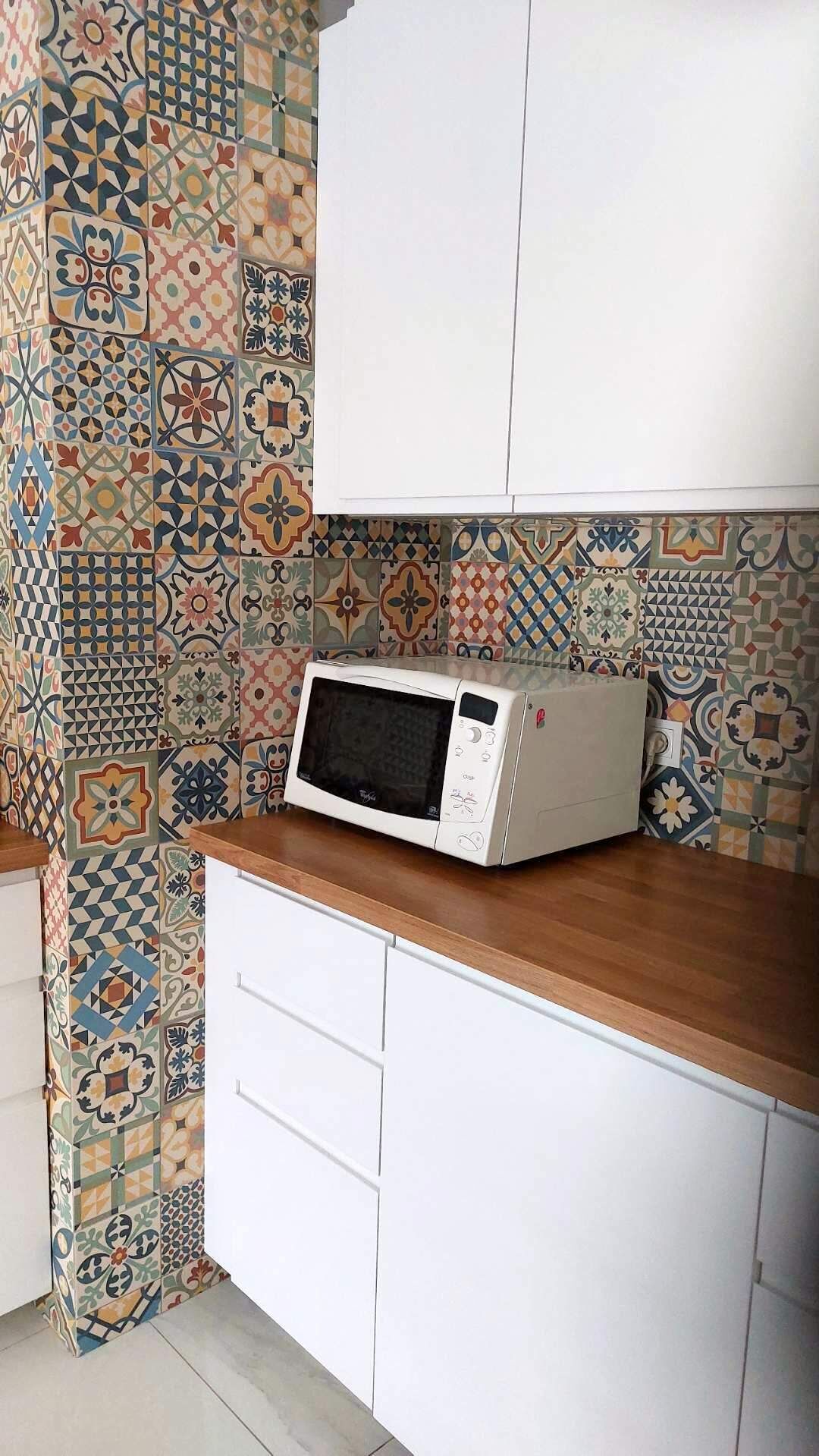 Cocina con microondas sobre encimera de madera, armarios blancos y salpicadero de azulejos con distintos diseños.