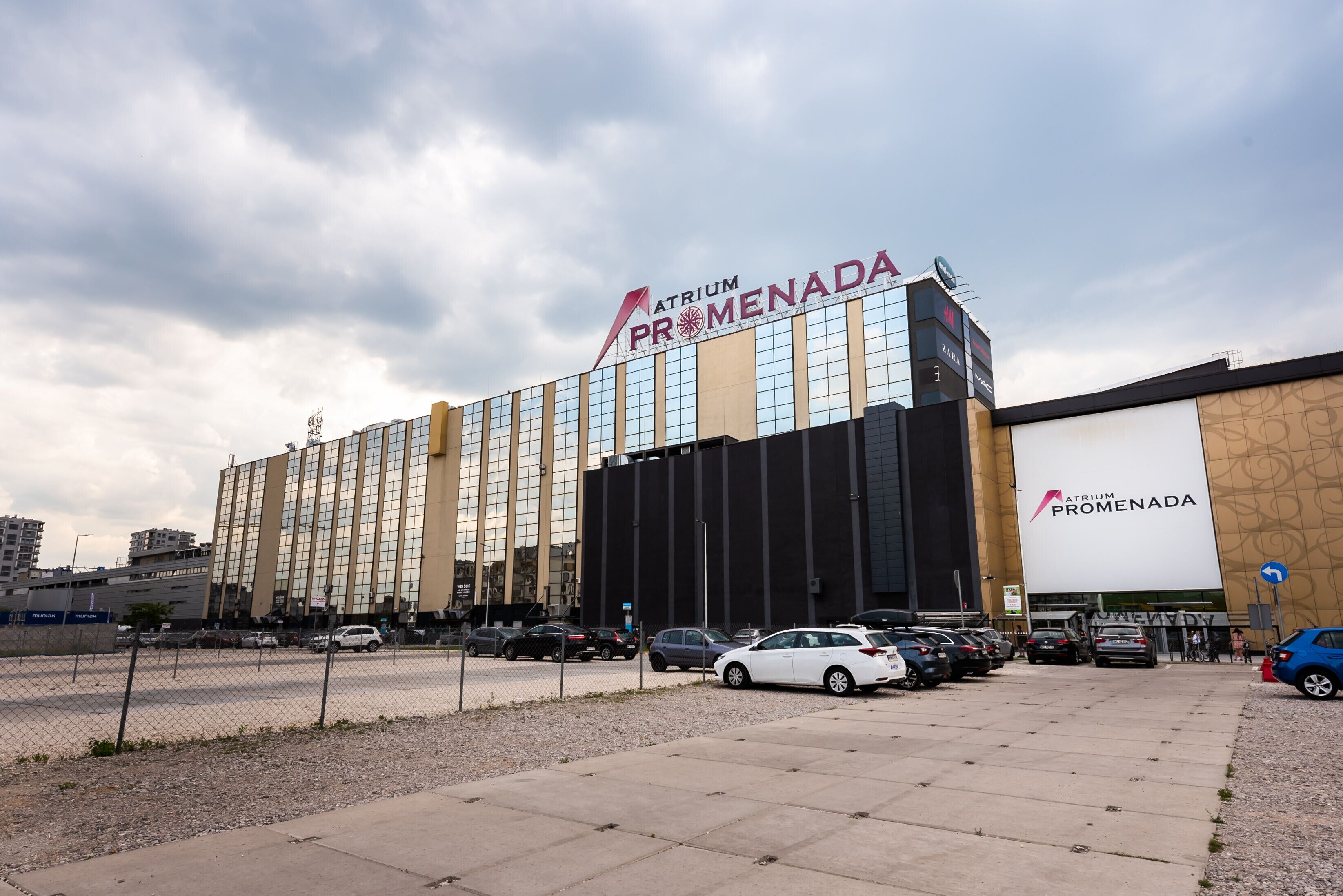 Un hotel grande con un llamativo letrero Atrium Promenada, con fachada de vidrio moderna y varios espacios de estacionamiento al frente.