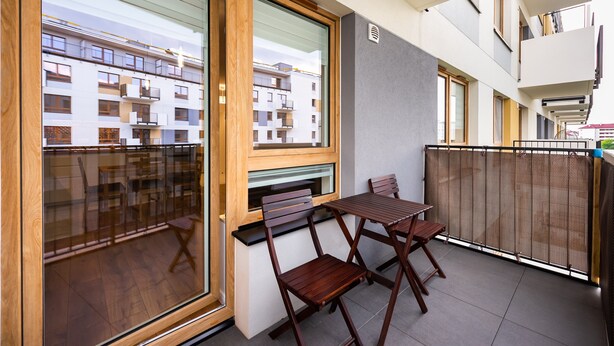 A balcony with a wooden table and chairs, a sliding glass door, and a view of a multi-story building.