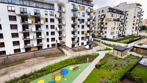 A multi-story residential building with balconies, a children's play area with colorful ground cover, and a landscaped garden.