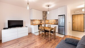 A modern kitchen with white cabinetry, a wooden dining table, and a built-in TV.