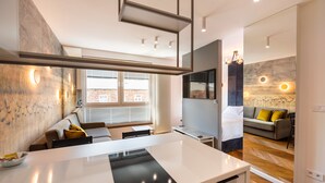 A modern kitchen with a central island, a dining area with a table and chairs, and a living area with a sofa and a TV. - Nowa Praga Geometric Yellow Apartment (Warszawa)