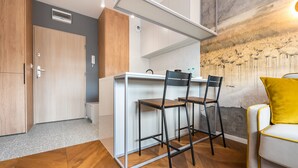 A compact room with a kitchenette, two chairs, a sofa with a yellow cushion, and a wall mural. - Nowa Praga Geometric Yellow Apartment (Warszawa)