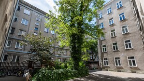 Rakennuksessa on useita ikkunoita, sen edessä kasvaa puu ja lähellä on pysäköitynä polkupyörä.