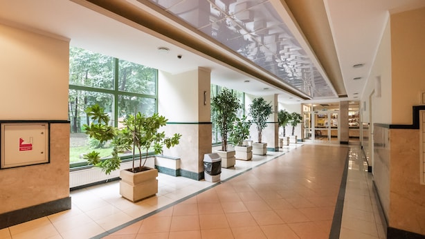 A spacious corridor with large windows, potted plants, and a clean tiled floor. - Ogród Saski Colored Studio (Warszawa)