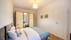 A bedroom with a bed, a mirror, a wardrobe, and a door. - Metro Plac Wilsona Etno Apartament (Warszawa)