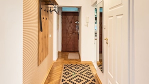 A hallway with a patterned carpet, a white cylindrical object, and a wooden door. - Metro Plac Wilsona Etno Apartament (Warszawa)