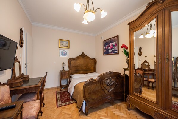 A bedroom with a wooden bed, a large mirror, a wooden dresser, a desk with a chair, and a television. - Downtown Antique Apartment (Warszawa)