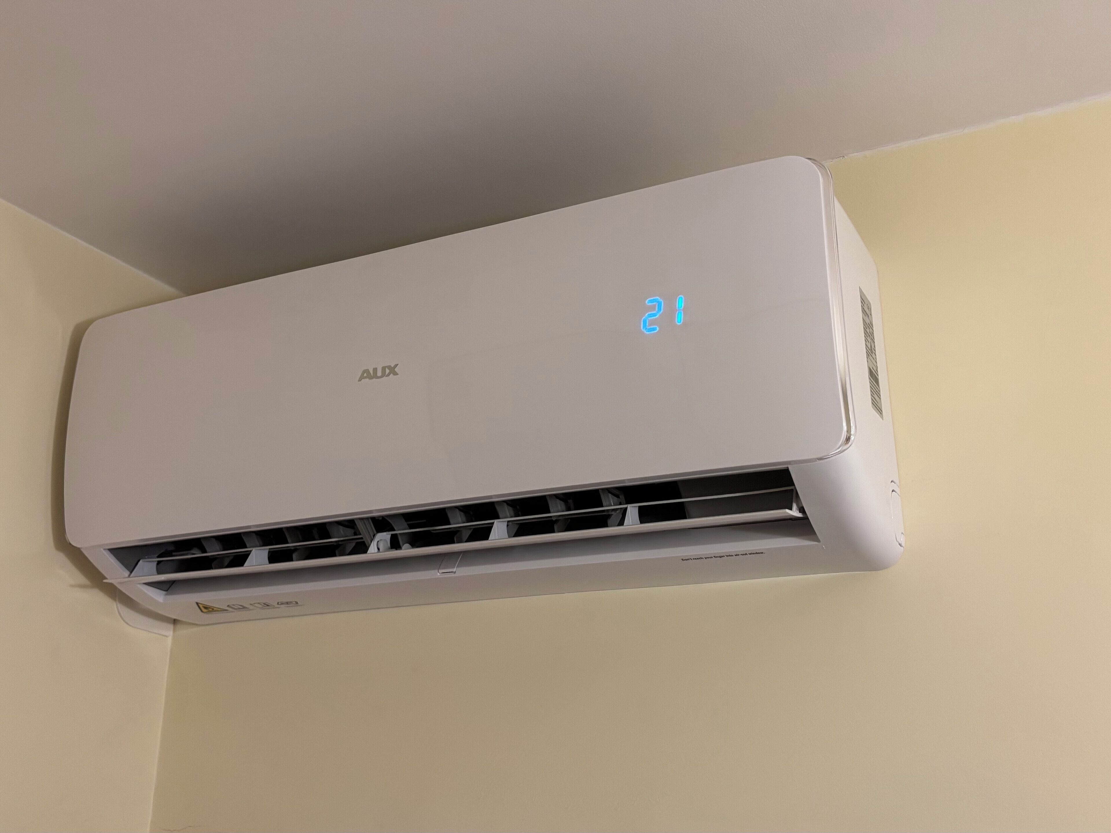 Un appareil de climatisation blanc de la marque « AUX », doté d’un écran numérique affichant le chiffre « 21 ».