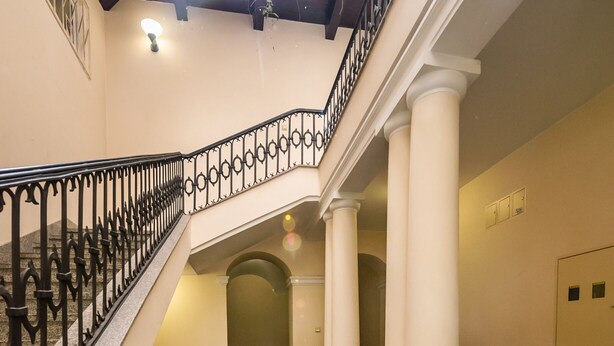 A multi-level interior with a central staircase, white columns, and black wrought iron railings. - Lovely Apartment In The Heart of Warsaw (Warszawa)