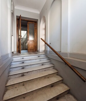 Un escalier avec une rampe en bois, une porte en bois en haut, et une vue sur un autre escalier menant à une autre pièce.