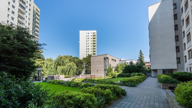 A pathway leading to a building with a modern design, surrounded by well-maintained greenery and a clear blue sky. - Metro Wilanowska Homely Apartment (Warszawa)