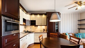 A modern kitchen with dark wood cabinets, a stainless steel oven, and a dining area with a wooden table and chairs. - Metro Wilanowska Homely Apartment (Warszawa)