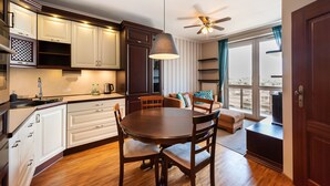 A modern kitchen with white cabinets, a dining table with chairs, a ceiling fan, and a large window with curtains. - Metro Wilanowska Homely Apartment (Warszawa)