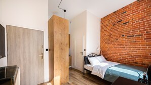 A bedroom with a wooden wardrobe, a bed with a brick wall, and a wooden floor. - National Stadium Cosy Studio #2 (Warszawa)