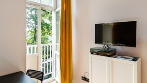 A room with a TV mounted on a cabinet, a dining table with chairs, and a large window with yellow curtains. - National Stadium Cosy Studio #2 (Warszawa)