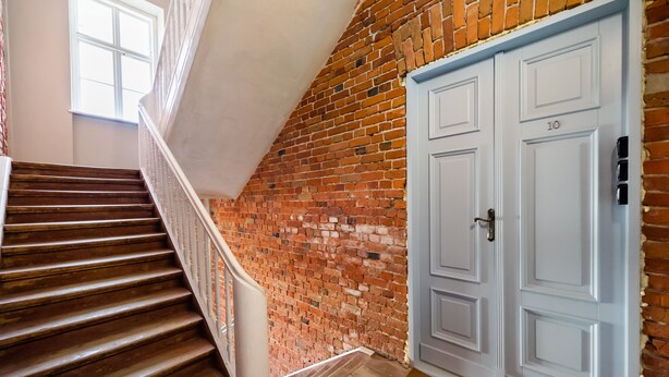 A staircase with wooden steps and a white railing, leading to a room with a brick wall and a light blue door marked with the number 10. - National Stadium Cosy Studio #3 (Warszawa)