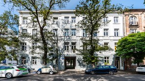 A multi-story building with a central entrance, surrounded by trees. There are parked cars in front. - National Stadium Cosy Studio #3 (Warszawa)
