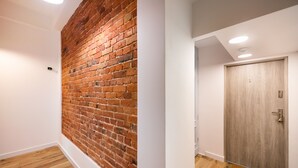 A hallway with a brick wall and wooden flooring, leading to a wooden door. - National Stadium Cosy Studio #3 (Warszawa)