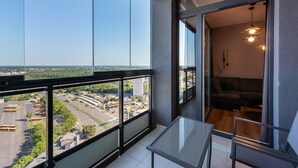 Un balcon avec une table en verre et un canapé, donnant sur un parking et des immeubles.