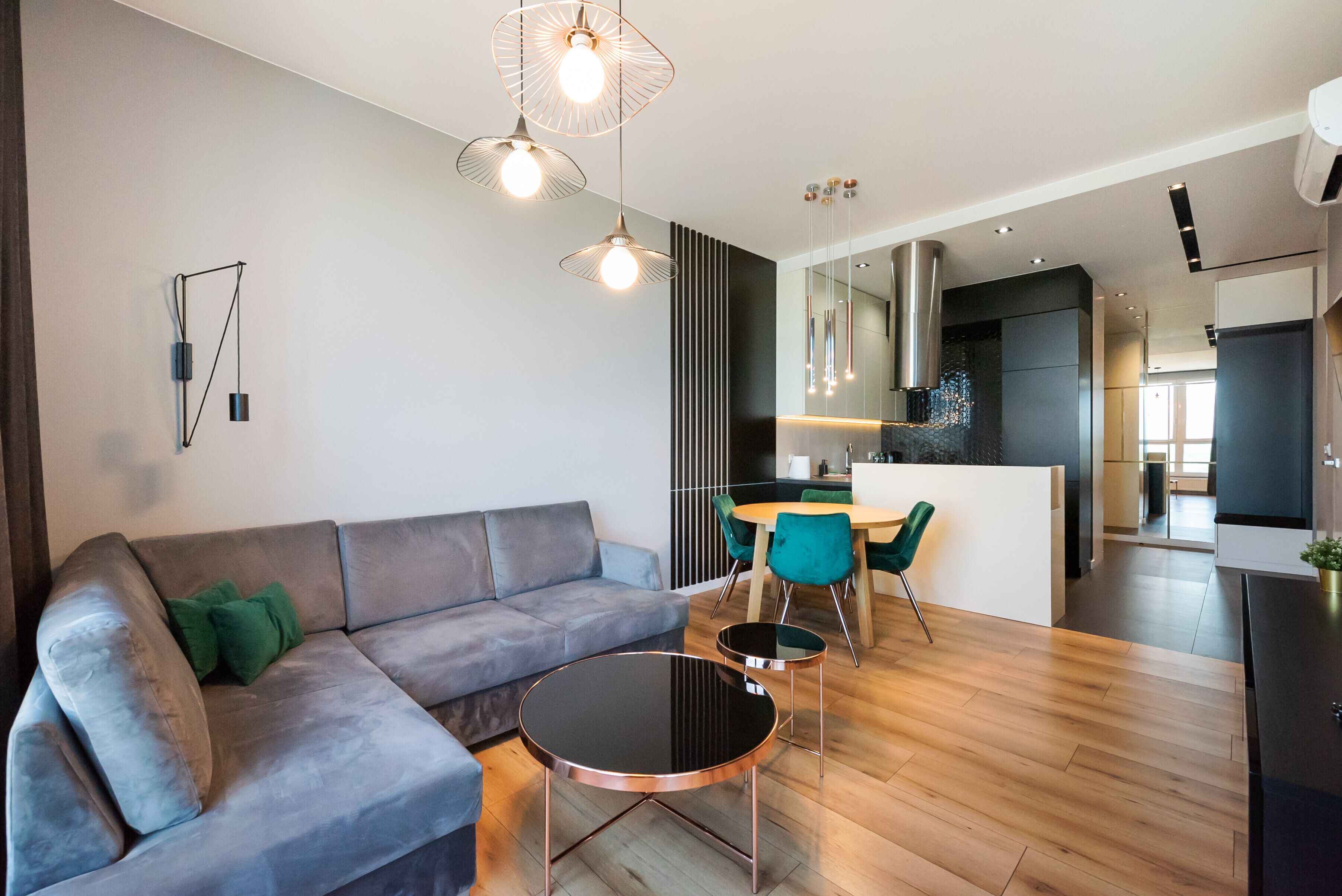 Ein modernes Wohnzimmer mit einem grauen Sofa, einem runden schwarzen Couchtisch und einem Essbereich mit einem grünen Sessel.