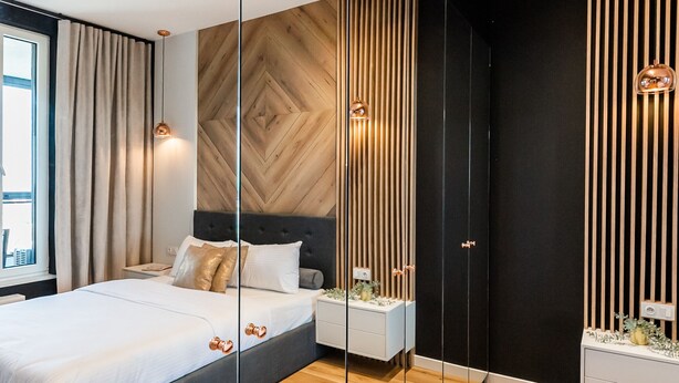 Une chambre moderne avec un lit, des tables de chevet, un miroir et un plancher en bois.