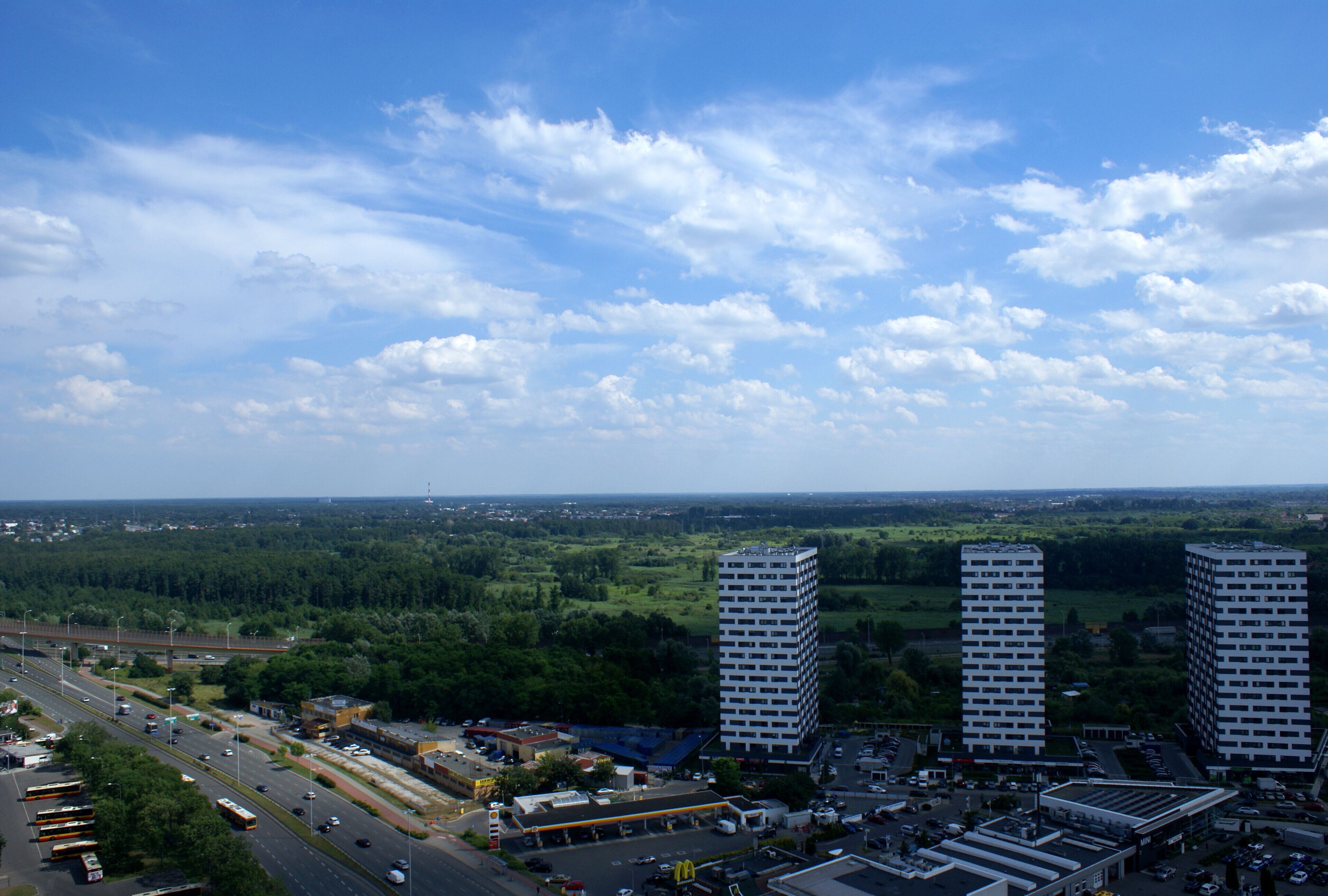 A cityscape with two prominent high-rise buildings, a highway, and surrounding greenery.