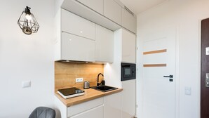 A compact kitchen with white cabinets, a wooden countertop, a black sink, and a modern light fixture.