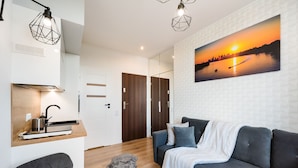 A modern living room with a grey sofa, a white throw blanket, and a painting of a sunset over a body of water.