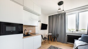 A modern kitchen with white cabinets, a black microwave, and a wooden countertop. There is a dining area with a small table and chairs, and a gray rug on the floor.