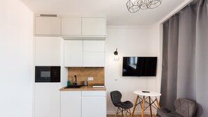 A compact kitchen with white cabinets, a microwave, and a wooden countertop. There is a dining area with two chairs and a small table. A flat-screen TV is mounted on the wall.