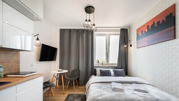 A modern hotel room with a bed, a desk, a chair, a TV, and a painting on the wall.