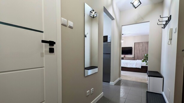 A hallway leading to a bedroom with a bed, a TV, and a mirror. - Ursus Pleasant Apartment (Warszawa)
