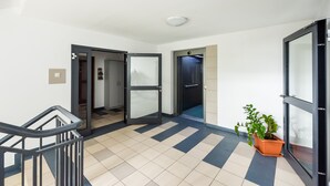A hallway with a tiled floor, a potted plant, and a staircase with a handrail. - Ursus Pleasant Apartment (Warszawa)