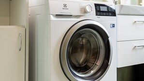 A front-loading washing machine with a control panel, stacked with folded towels, in a modern bathroom with a tiled backsplash and a white cabinet. - Ursus Pleasant Apartment (Warszawa)