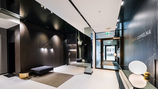 A modern lobby with a bench, a reception desk, and a glass door leading to apartments. - Złota Sophisticated Apartment (Warszawa)