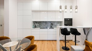 A modern kitchen with white cabinets, a marble backsplash, and a black countertop. There are two black bar stools and a glass table with a woven placemat. - Złota Sophisticated Apartment (Warszawa)