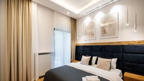 A modern hotel room with a large bed, wooden headboard, and a view of the outdoors. - Złota Sophisticated Apartment (Warszawa)