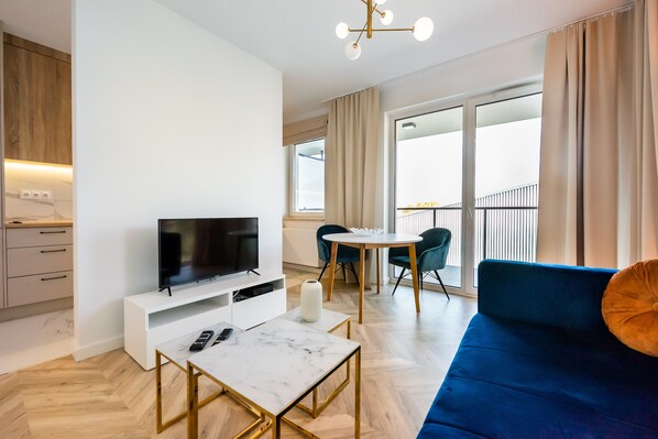A modern living room with a TV, a white coffee table, a blue sofa, and a dining area with a table and chairs. - East Side of Warsaw Studio 111 (Warszawa)