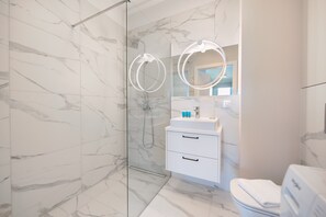 A modern bathroom with marble walls, a glass shower enclosure, a white sink with a mirror, and a toilet. - East Side of Warsaw Studio 111 (Warszawa)