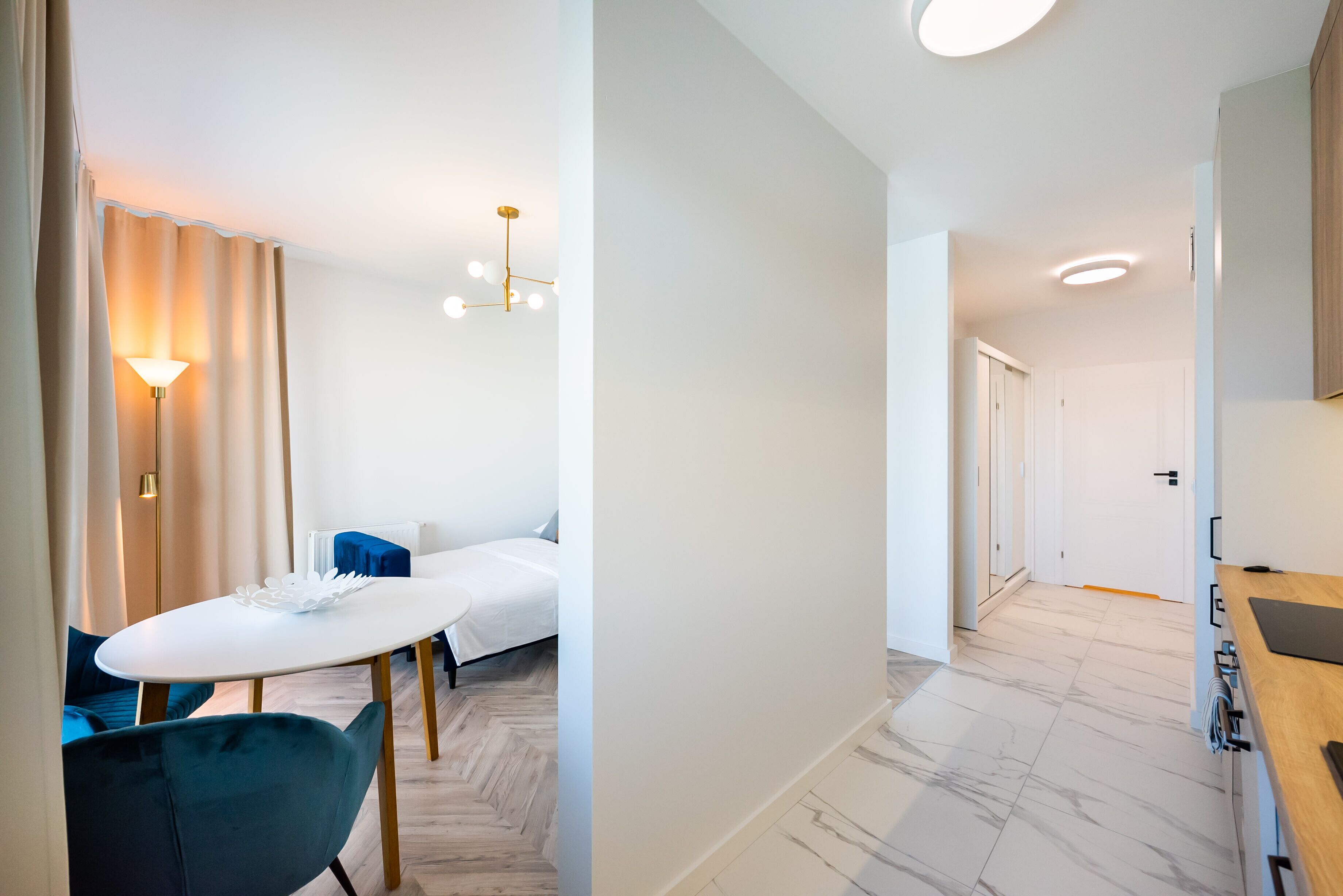 A modern hotel room with a dining area, a bed, and a hallway leading to another room.