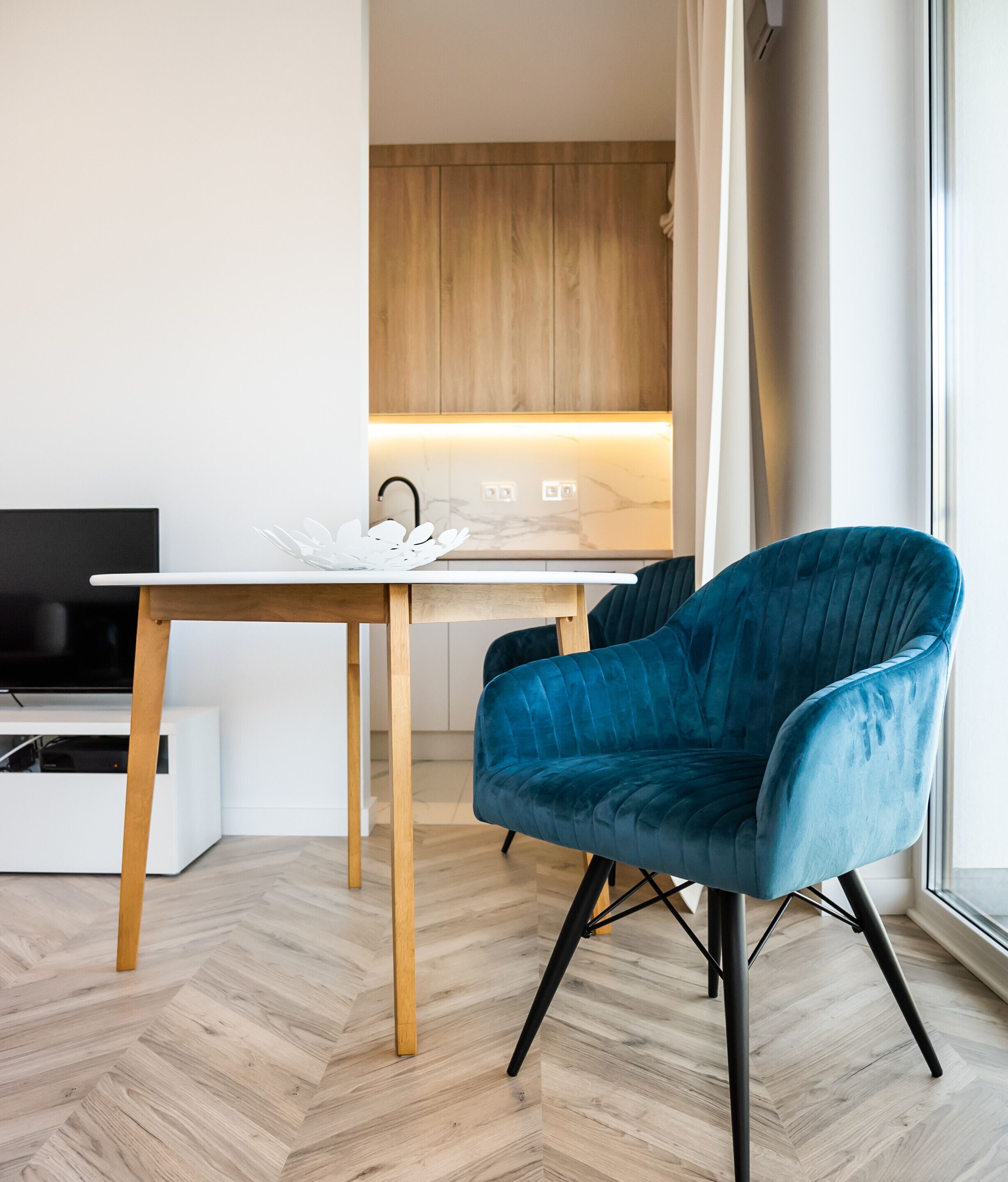 A modern kitchen with wooden cabinets, a white countertop, and a blue chair.