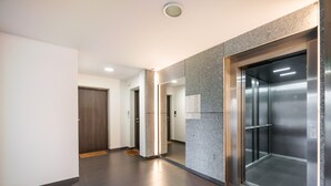 A modern elevator with a metallic finish, a hallway with a marble wall, and a wooden door. - Służewiec Comfort Zone Apartment (Warszawa)
